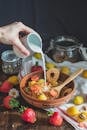 A Person Pouring Milk into a Bowl with Cereal and Fruit
